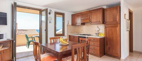 A kitchen with wooden cabinets, a dining table with chairs, a refrigerator, and a view of the outside.