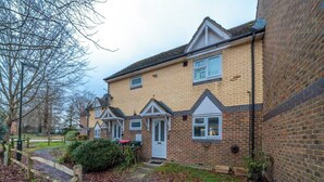 A two-story residential building with a brick facade, a front door, and a small front yard with a wooden fence and a pathway. - Gatwick Layover: Modern 1BR Free Parking & Garden (Crawley)