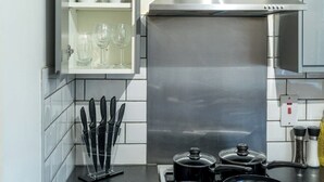 A kitchen with white tiled walls, a stainless steel range hood, a pot on the stove, and a knife block. - Gatwick Layover: Modern 1BR Free Parking & Garden (Crawley)