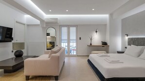 Ein modernes Hotelzimmer mit einem großen Bett, einer Couch, einem Fernseher und einem Balkon mit Blick.
