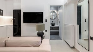 Ein modernes Hotelzimmer mit einer Couch, einem Fernseher, einer Lampe und einem durch eine offene Tür einsehbaren Badezimmer.