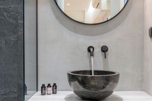 Ein modernes Badezimmer mit einem großen, dunkel marmornen Waschtisch, zwei Wasserhähnen und einem Spiegel darüber.