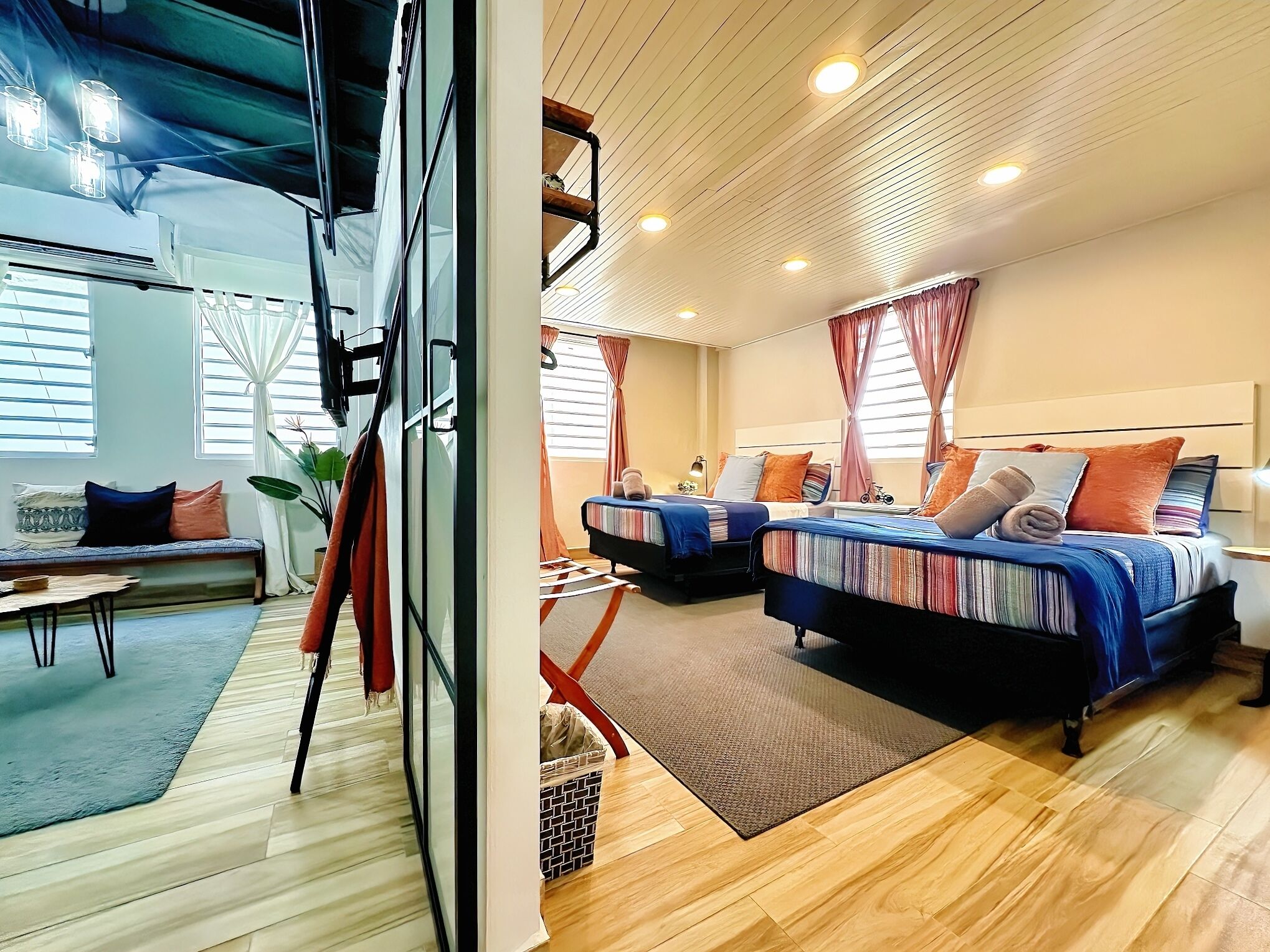 Ein modernes Hotelzimmer mit zwei Betten, einem Sofa, einem kleinen Tisch und einem großen Fenster mit Vorhängen.