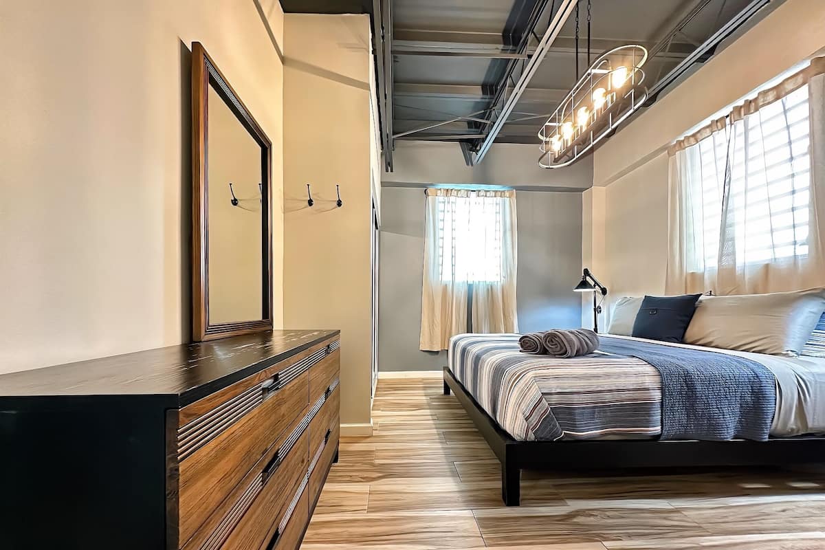 A bedroom with a wooden dresser, a bed with striped bedding, and a large mirror.