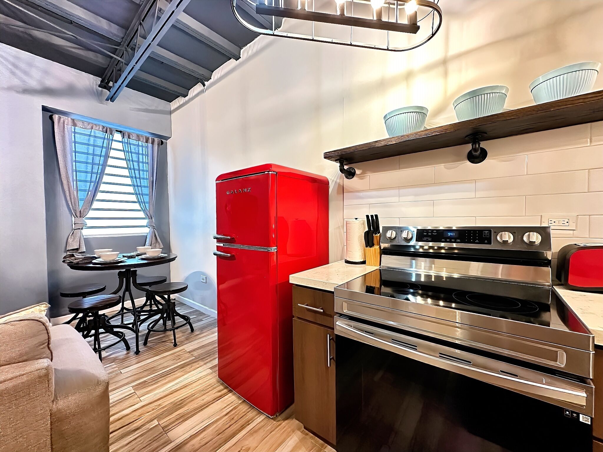 A compact kitchen with a red refrigerator, stainless steel stove, and a small dining area with a table and chairs.