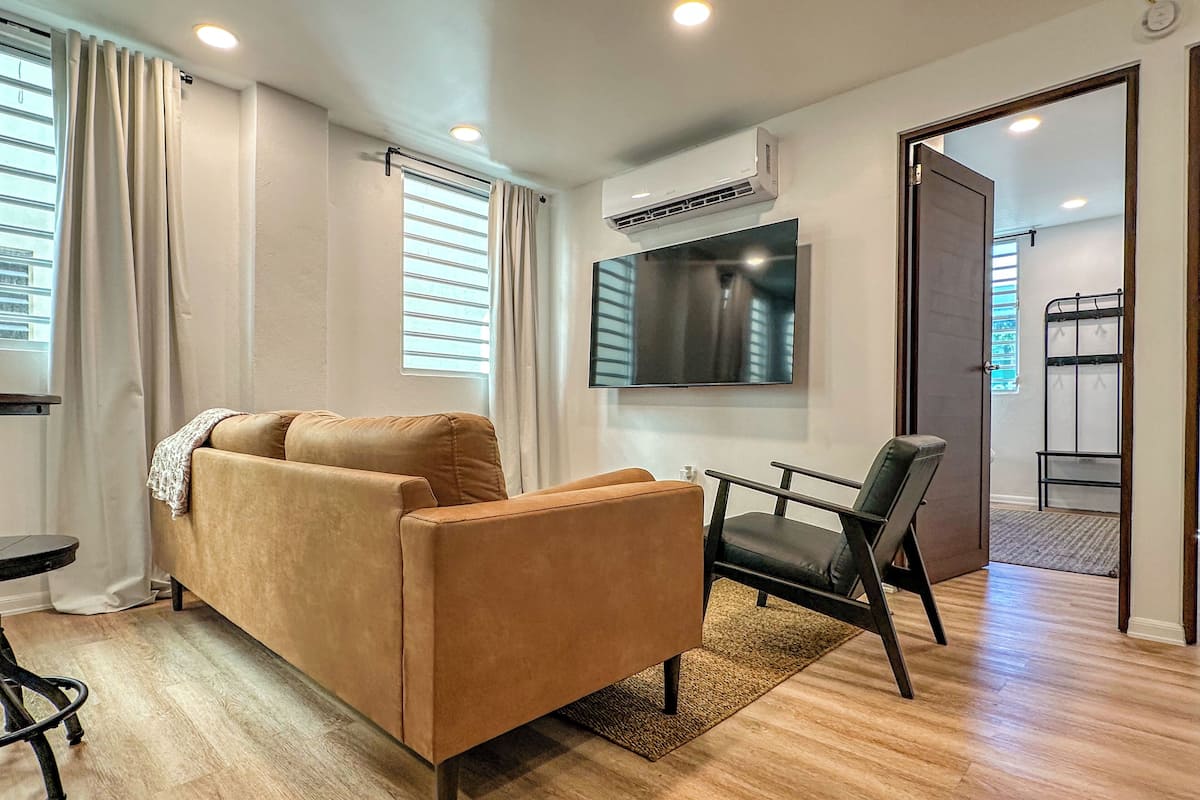 A modern living room with a sofa, a chair, a TV, and an air conditioning unit.
