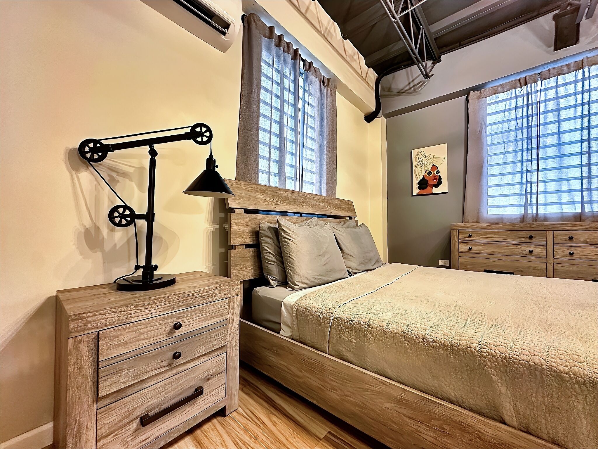 A bedroom with a wooden bed, a nightstand with drawers, a lamp, and a window with curtains.