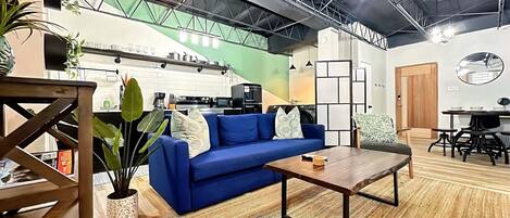 Un espacio habitable moderno con un sofá azul, una mesa de centro de madera y una cocina al fondo.