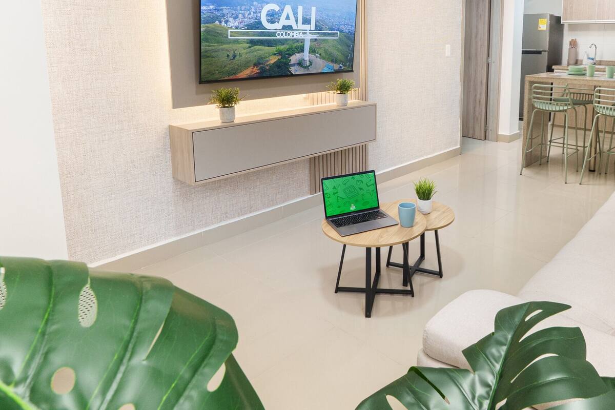 A modern living room with a flat-screen TV mounted on the wall, a laptop on a small table, and a sofa with green upholstery.