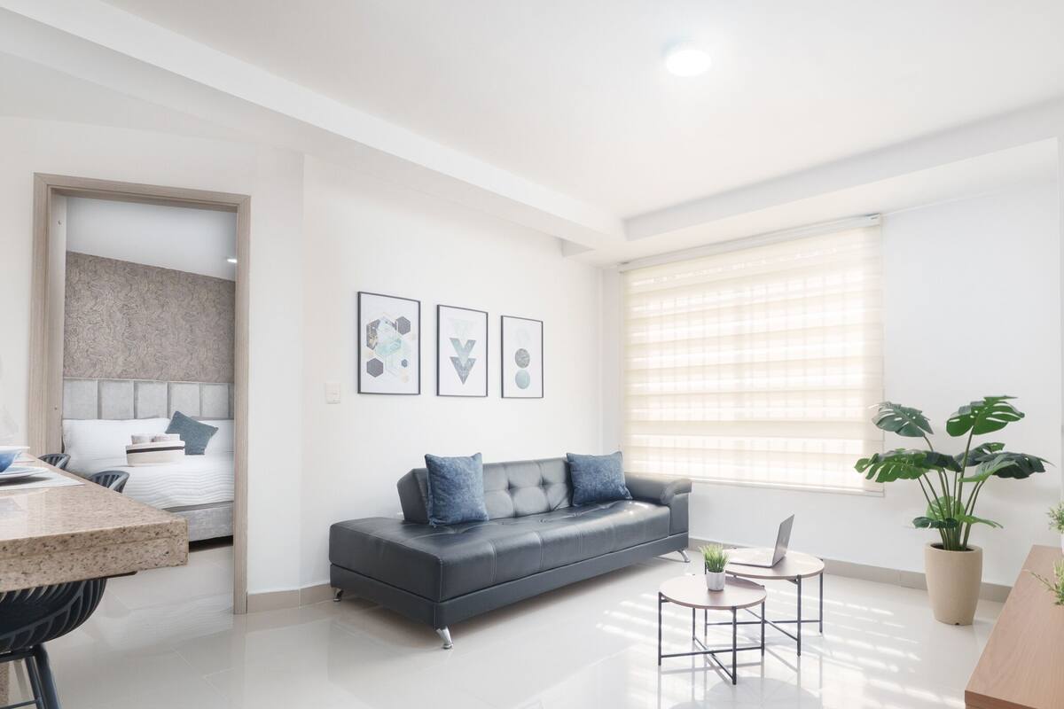 A modern, well-lit living room with a grey sofa, a small round table, and a potted plant.