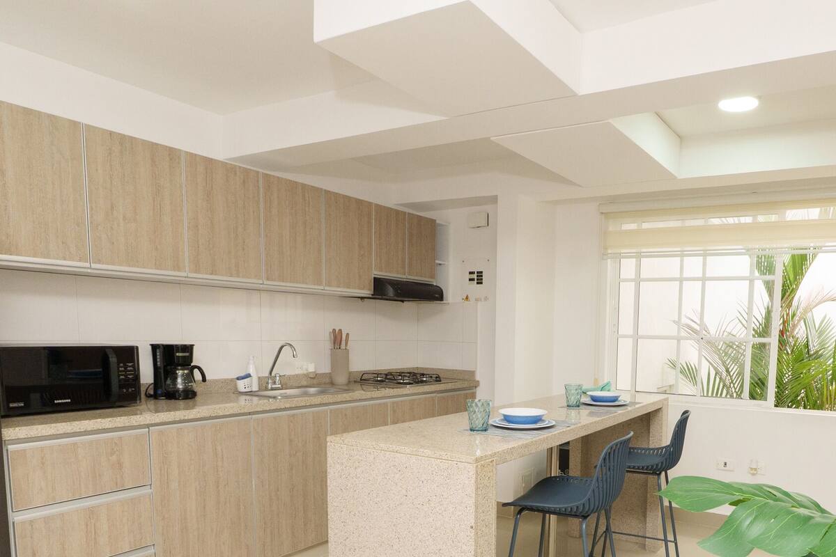 A modern kitchen with wooden cabinets, a gas stove, a microwave, and a window with a view of greenery.