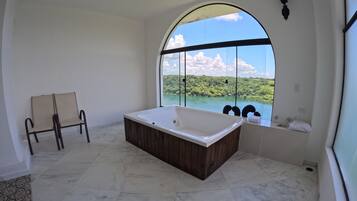 A spacious bathroom with a large bathtub, a window with a view of a lake and greenery, and a chair.