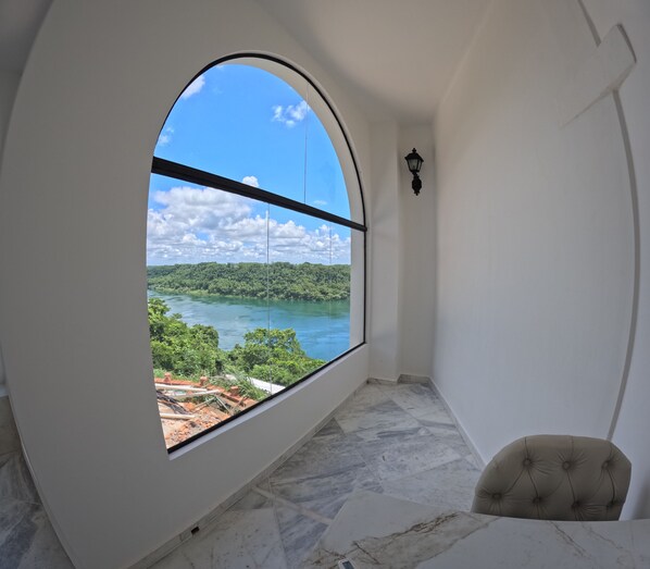 A room with a large arched window offering a view of a lake and forest. - Hotel Casablanca Boutique Swiss Bonmont (Hernandarias)