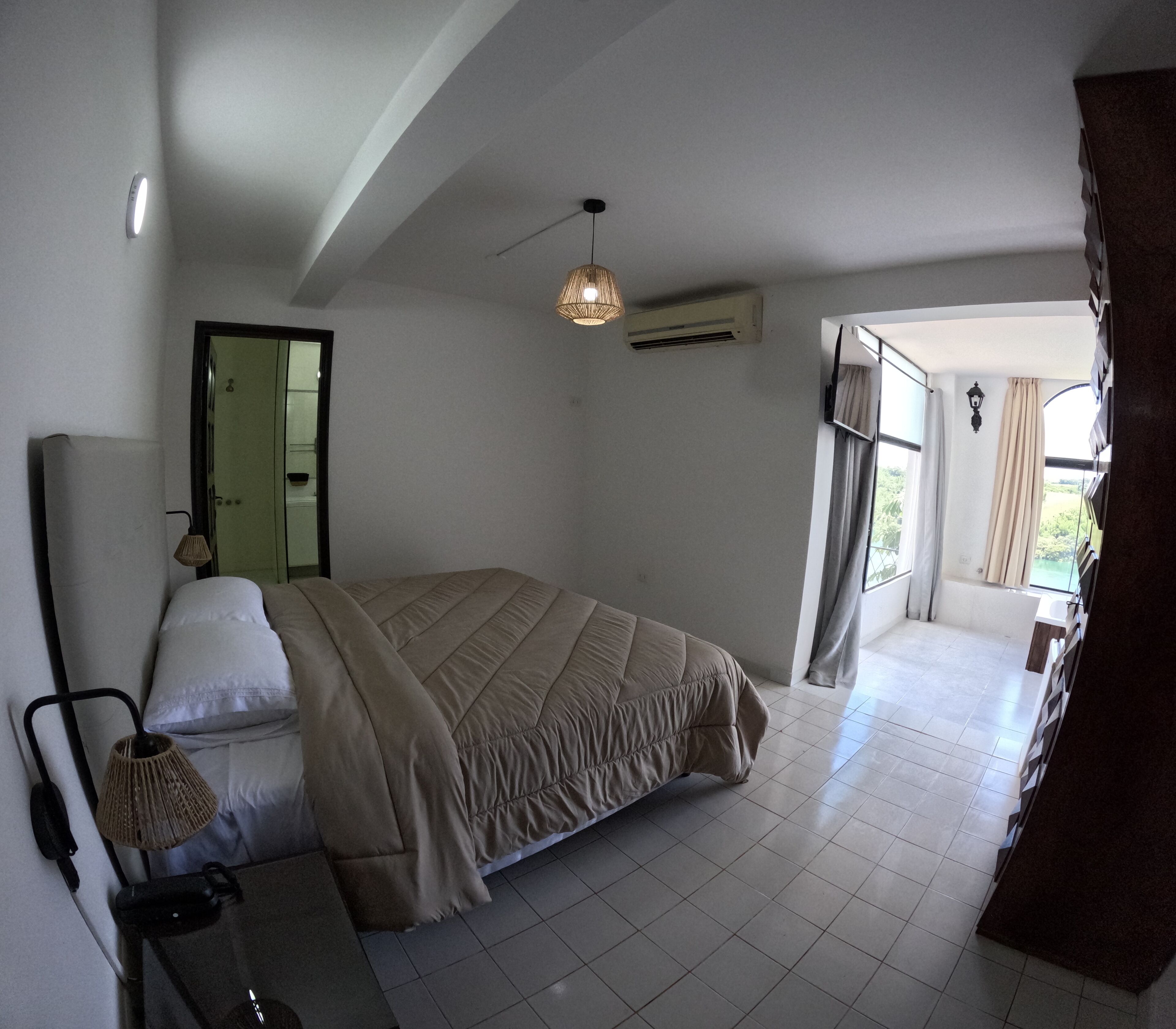 A bedroom with a bed, a bedside lamp, a mirror, and a window with curtains.