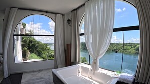 A modern bathroom with a large bathtub, two windows with curtains, and a view of a lake and greenery. - Hotel Casablanca Boutique Swiss Bonmont (Hernandarias)