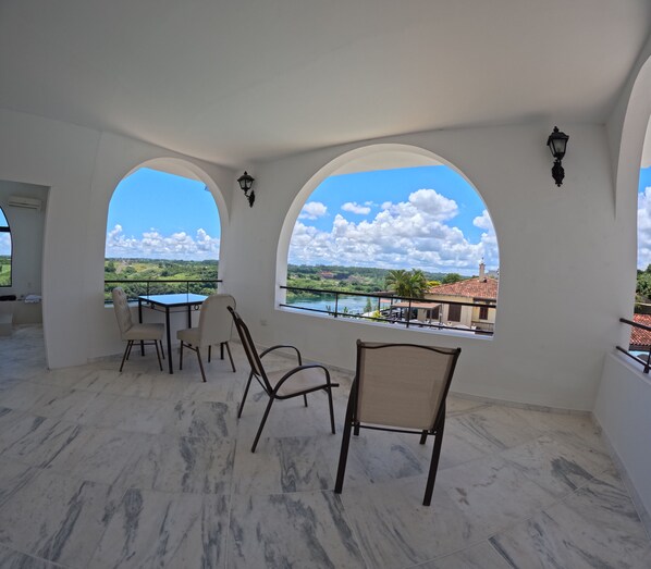 A spacious balcony with a marble floor, two arched windows offering a view of a river and greenery, and a table with chairs. - Hotel Casablanca Boutique Swiss Bonmont (Hernandarias)
