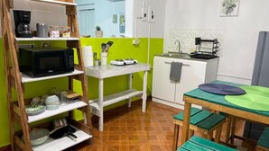 Una cuina compacta amb un moble de prestatges de fusta, un microones, un nevera petita i una taula de dinar amb bancs.
