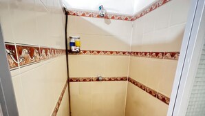 Un bany petit i amb rajoles, amb un vàter i una ampolla de xampú penjada a la paret.