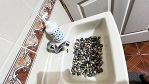 Un lavabo amb un dosificador de sabó, un robinet i un plat de pedres.