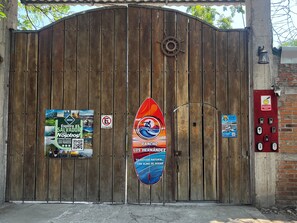 A wooden gate with a surfboard sign, a QR code, and a no parking sign.