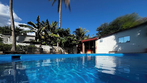 Una piscina azul cristalina con sillas de descanso y un edificio con tejado rojo al fondo.