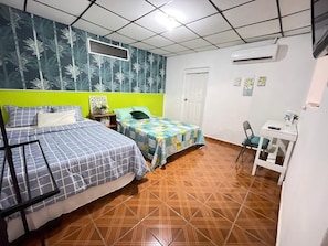 A room with two beds, a desk, and an air conditioning unit.