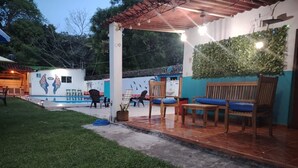 Un patio exterior con sillas y una mesa, un mural con aves y una piscina al fondo.