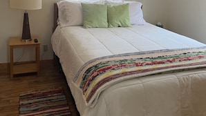 Une chambre à coucher avec un lit, une table de chevet avec une lampe, un ventilateur de plafond et une fenêtre avec des stores.