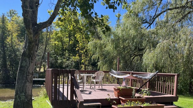Une terrasse en bois, agrémentée de meubles d’extérieur, notamment des chaises et un hamac, et entourée de verdure et d’arbres.