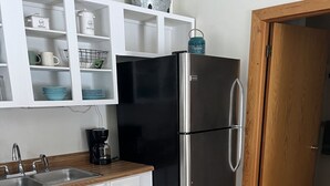Une cuisine de taille réduite avec des meubles blancs, un réfrigérateur en acier inoxydable, une machine à café et un tapis à carreaux.