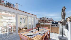 An outdoor dining area with a table set for four, a grill, and a view of the city.
