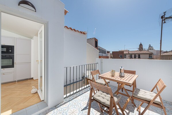 A balcony with a wooden table and chairs, a view of the cityscape, and a kitchen with modern appliances.