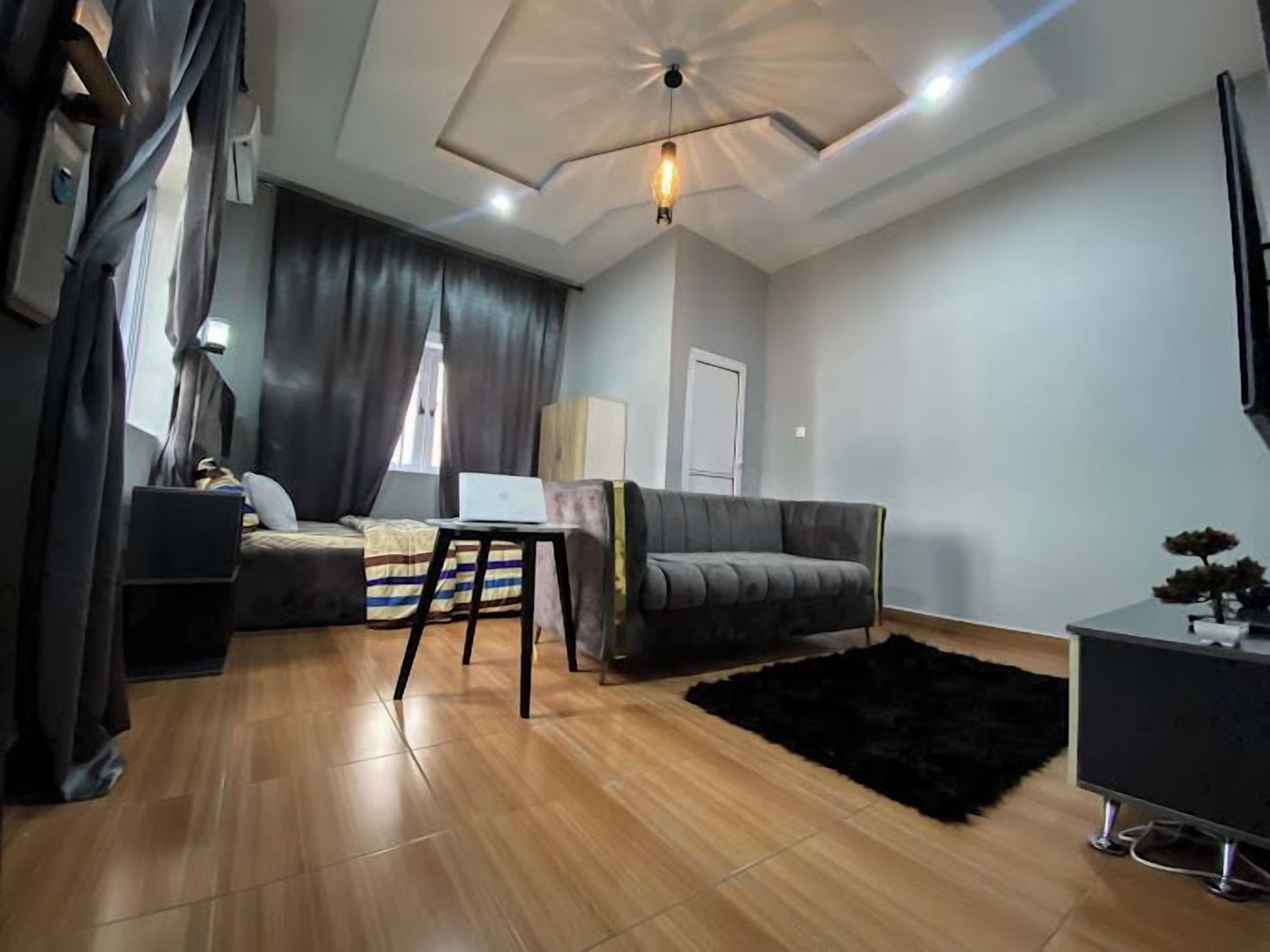 Una sala de estar moderna con un sofá gris, una mesita con una computadora portátil, un tapete negro y un mueble para televisión.