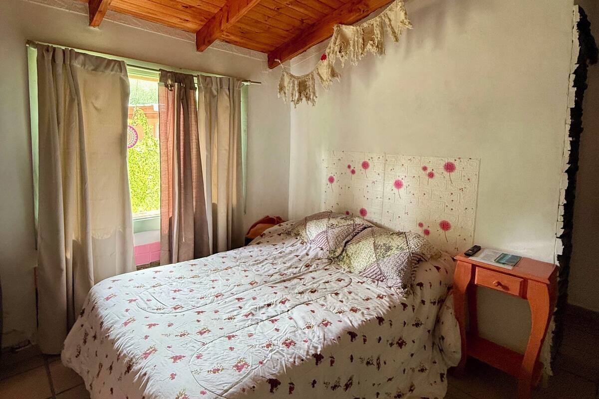 A bedroom with a bed, curtains, a wooden headboard, a bedside table, and a window.