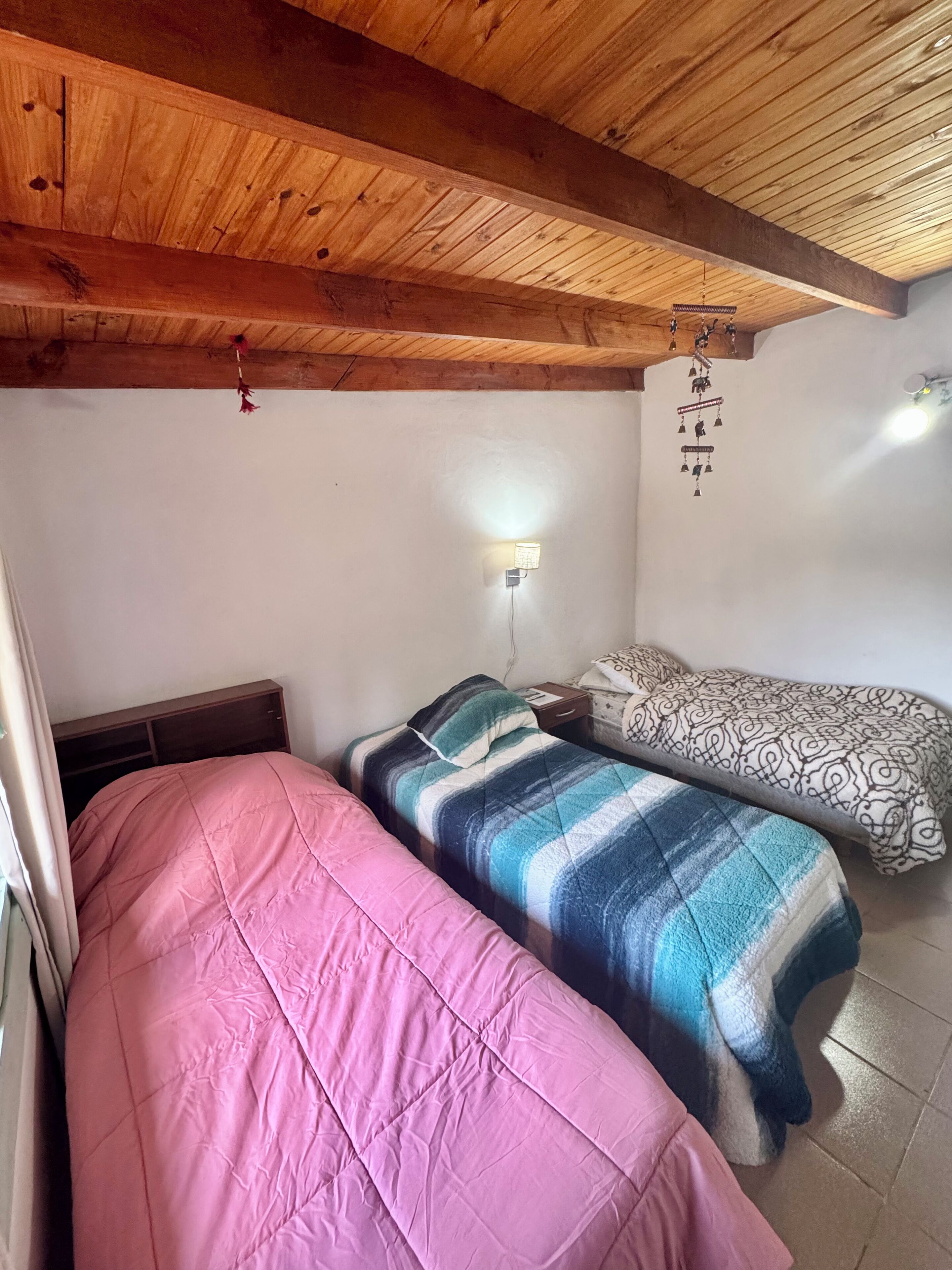 Ein Zimmer mit zwei Betten, Holzbalkendecke, einer Wandleuchte und einer hängenden Dekoration.
