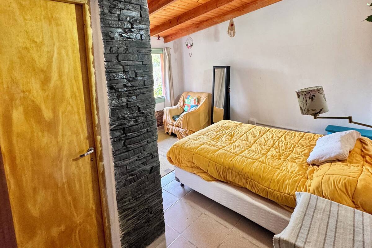 A bedroom with a bed, a chair, a stone wall, and a wooden ceiling.