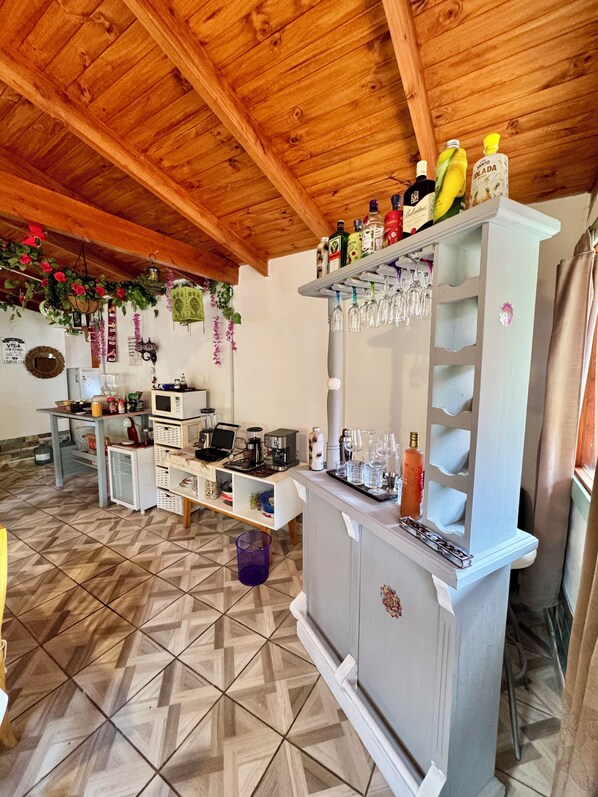 A kitchen with a wooden ceiling, a refrigerator, a sink, a microwave, and a shelf with bottles and glasses. - Mama Eva House (Lago Puelo)
