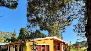 A yellow building with a red roof, surrounded by greenery and trees. - Mama Eva House (Lago Puelo)