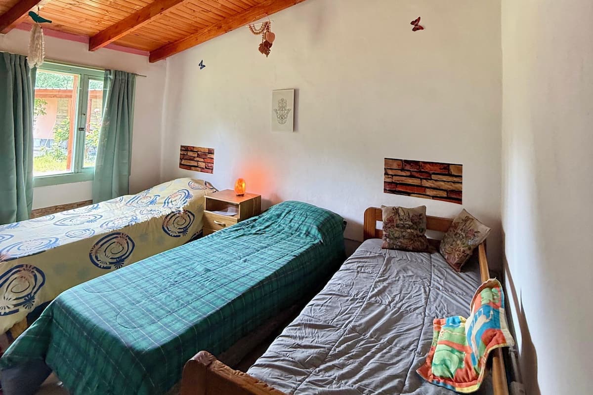 A room with two single beds, wooden headboards, a window with curtains, and a wall-mounted light.