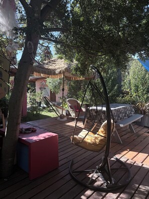 A wooden deck with a swing chair, a bench, and a table with a patterned tablecloth. - Mama Eva House (Lago Puelo)