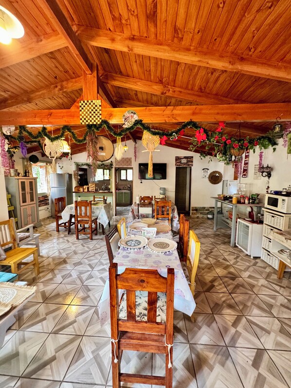 A dining area with a long table, chairs, and a kitchen in the background. - Mama Eva House (Lago Puelo)