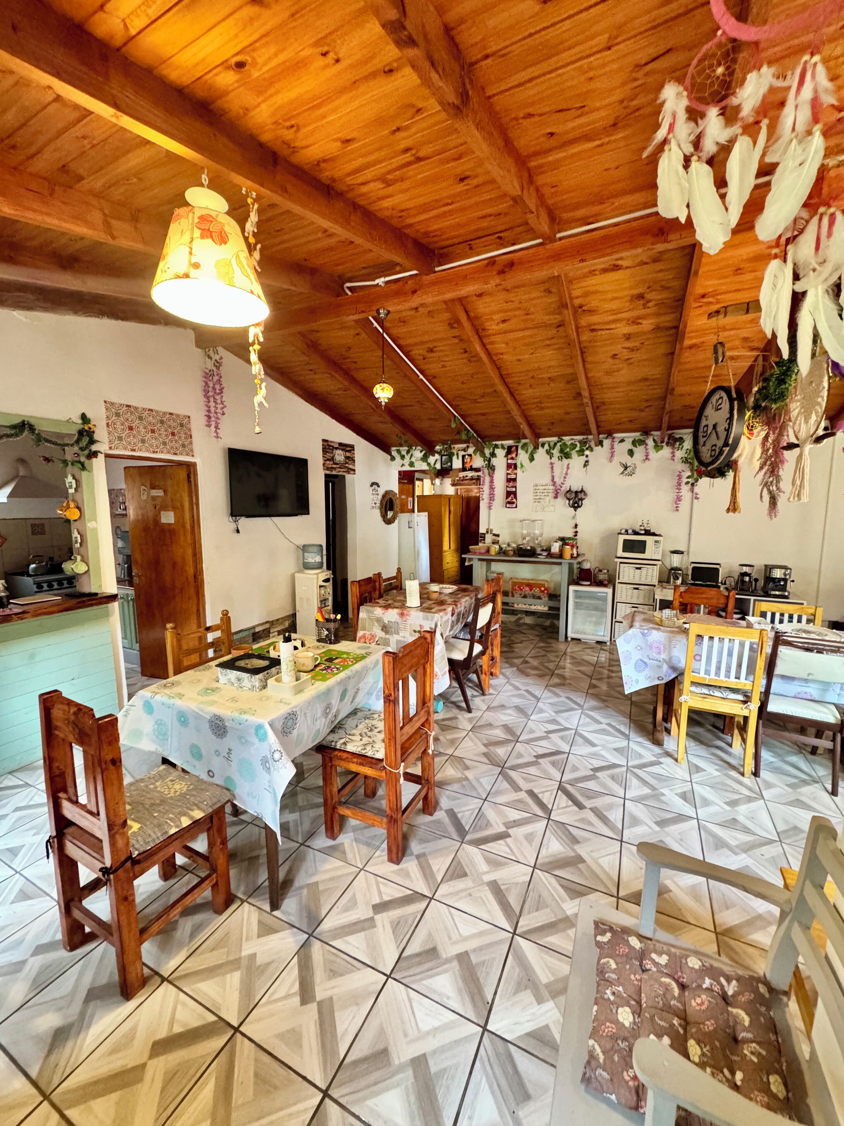 Un coin repas avec des chaises en bois et une table dressée pour quatre personnes, un espace cuisine équipé d’appareils électroménagers, et un plafond orné de poutres en bois et de décorations suspendues.