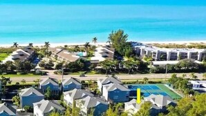 Un complejo turístico en la costa con edificios de varios pisos, una playa y una cancha de tenis.