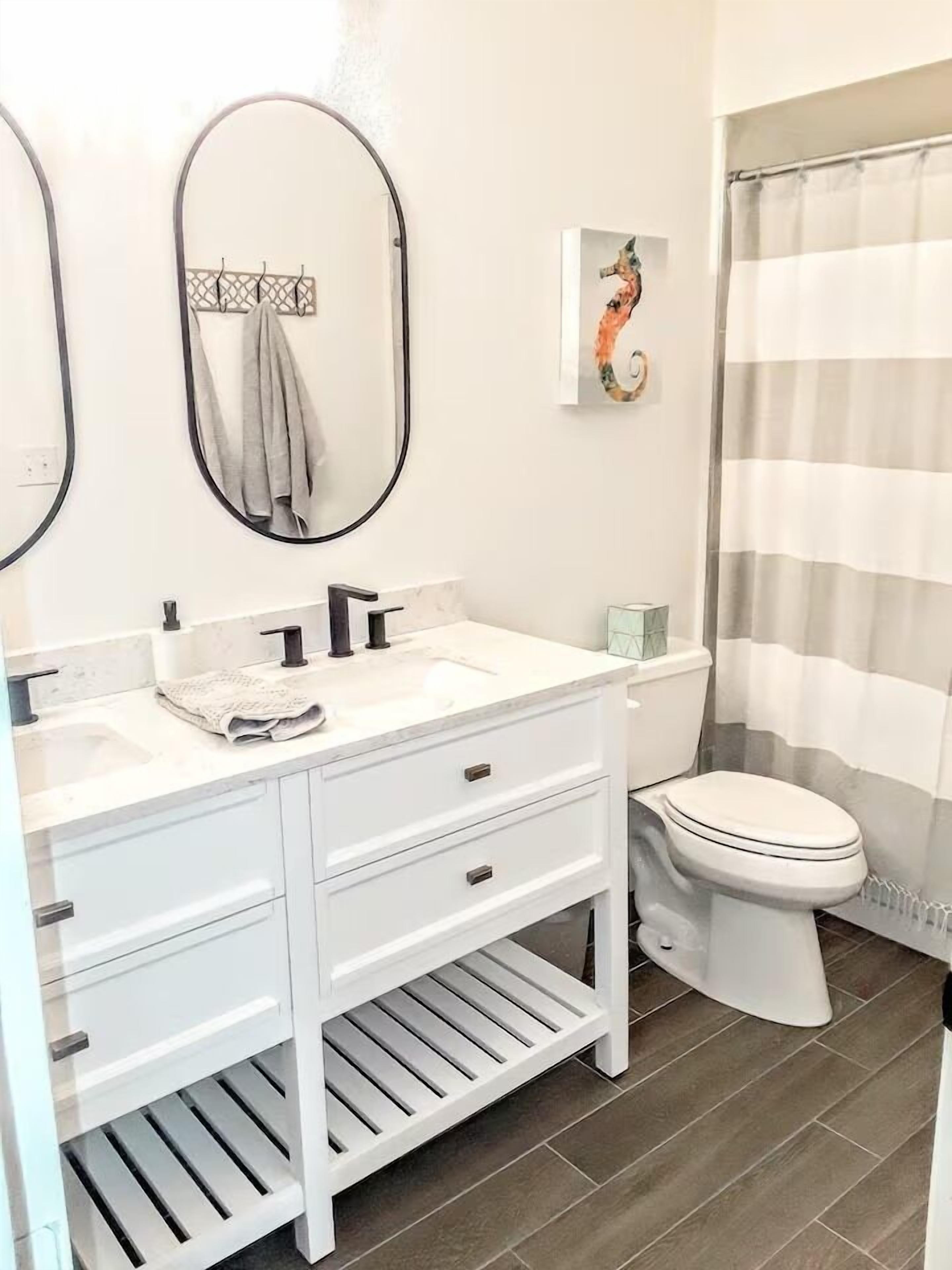 A bathroom with a white vanity, two mirrors, a toilet, and a shower curtain.