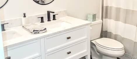 A bathroom with a white vanity, two mirrors, a toilet, and a shower curtain.