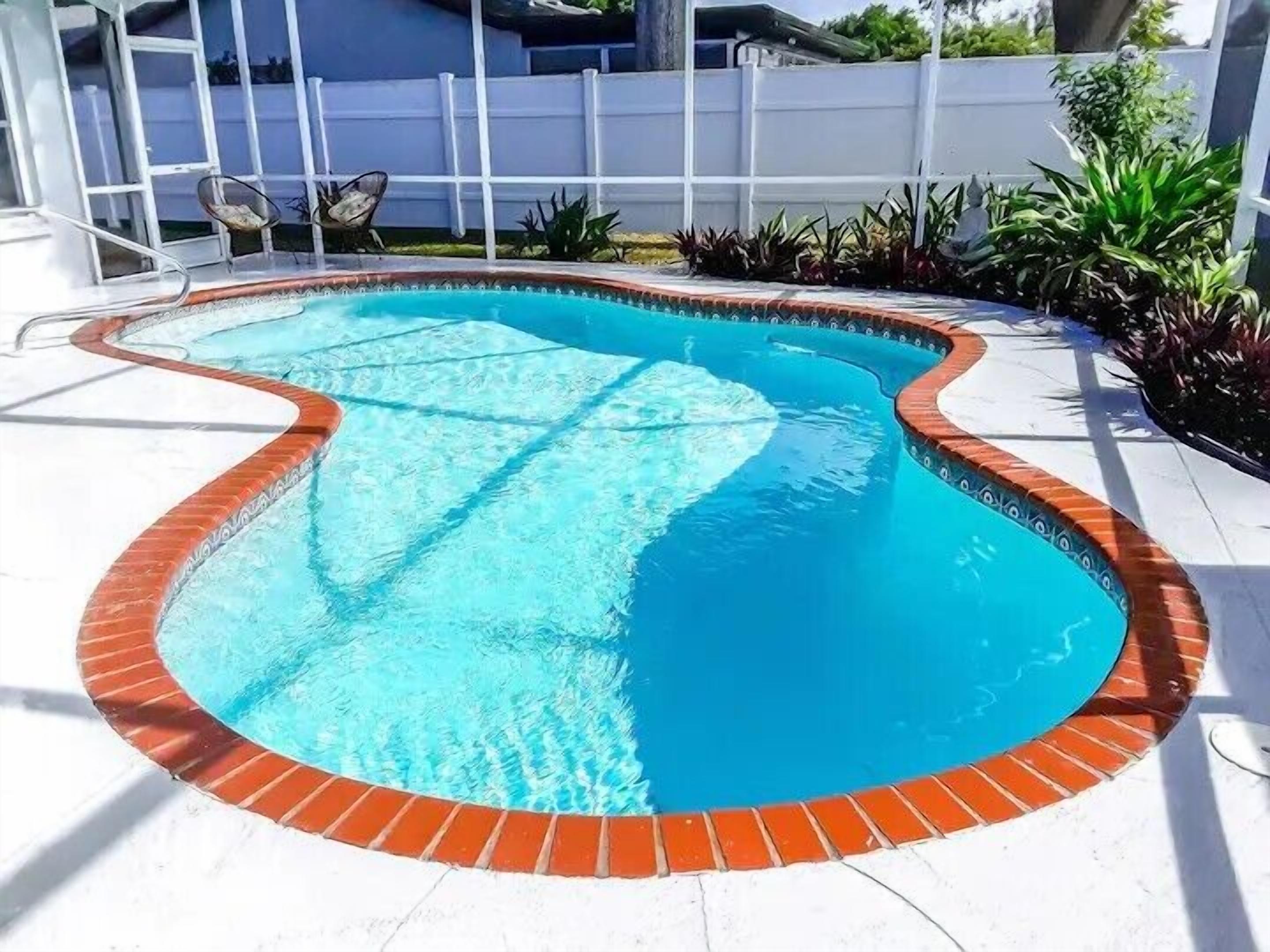 A swimming pool with a brick border and a white deck surrounding it.