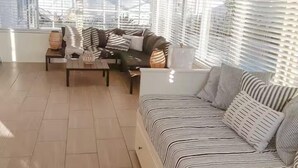 A sunlit living room with a sofa, coffee table, and a view through large windows.
