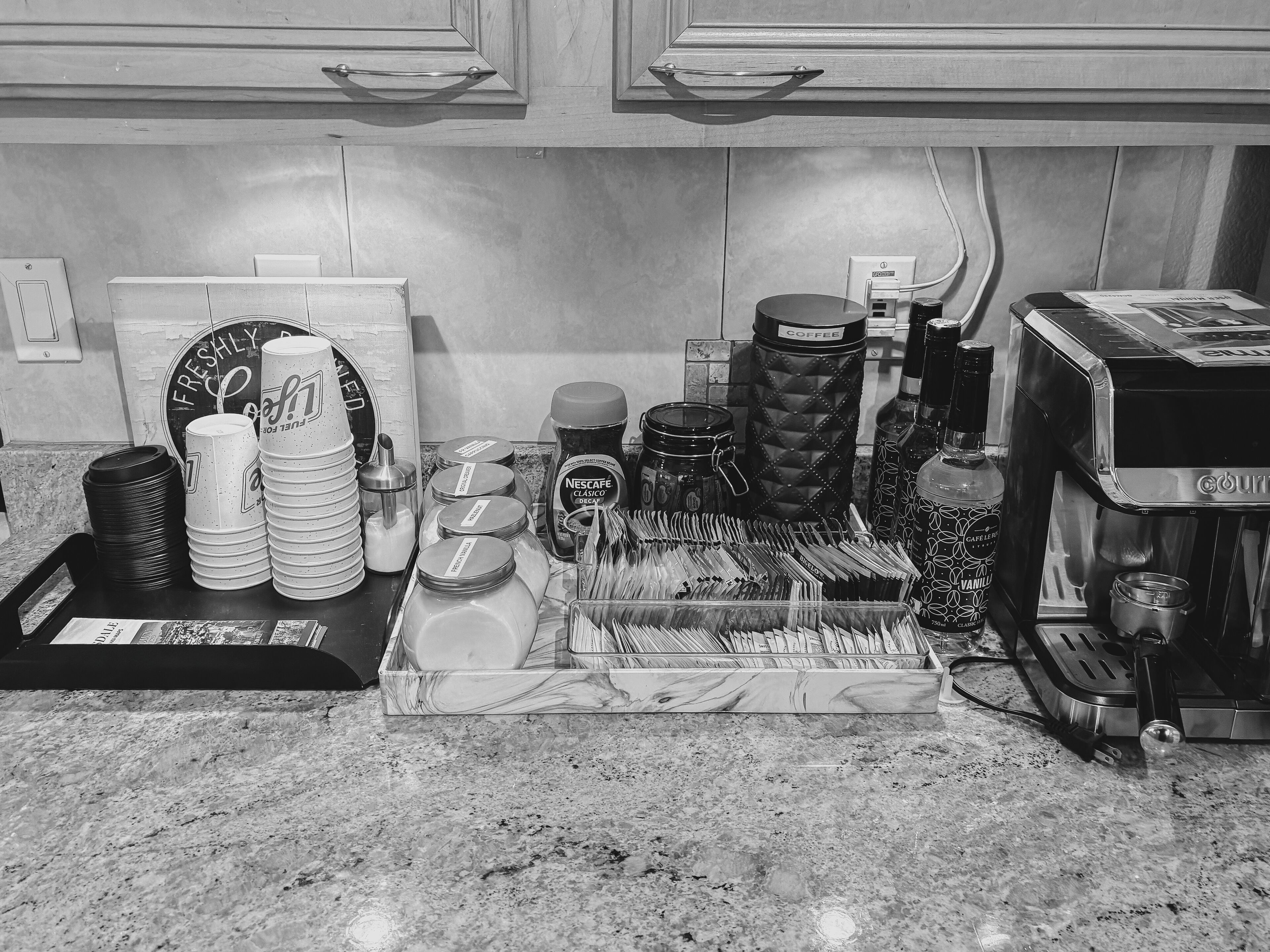 A kitchen counter with coffee-making equipment, including a coffee machine, cups, and a tray of utensils.