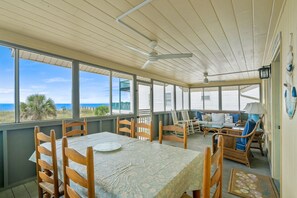A covered outdoor area with a table and chairs, large windows, and a ceiling fan. - Oceanfront Beach House in Ocean Drive. LOTS of Charm and amazing views! (North Myrtle Beach)