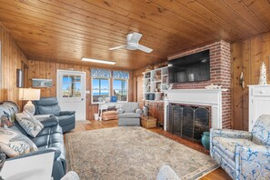 A cozy living room with a fireplace, leather sofas, a ceiling fan, and wooden walls.